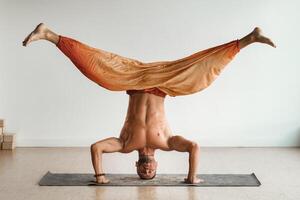 un' uomo con un' nudo torso fa yoga in piedi su il suo testa al chiuso. fitness allenatore foto