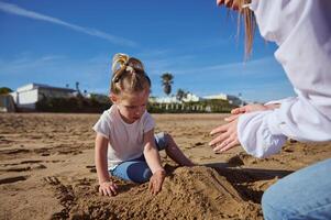 famiglia costruisce un' sabbia castello su il spiaggia su un' soleggiato giorno, contro il sfondo di il mare e il cielo con nuvole. foto