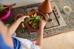 superiore Visualizza di un' donna casalinga mettendo fresco verde fagioli su la verdura, cottura a vapore nel tagine argilla pentola foto