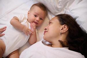 contento giovane madre e bambino bambino ragazzo dire bugie insieme su il letto foto
