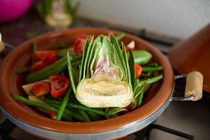un' metà di maturo biologico verde carciofo e verdure su il argilla piatto mentre cucinando tradizionale marocchino tagine foto