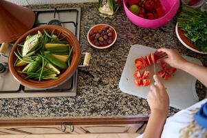 avvicinamento Visualizza di un' casalinga, donna capocuoco cucinare Tenere un' cucina coltello, affettare fresco rosso pomodori su un' taglio tavola foto