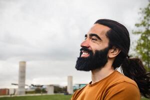 contento barbuto uomo con lungo capelli avendo divertimento sorridente nel un' parco foto