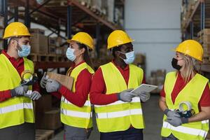 squadra Lavorando insieme nel magazzino fare inventario utilizzando digitale tavoletta e Caricamento in corso consegna scatole mentre indossare viso maschera durante corona virus scoppio - logistica e industriale concetto foto