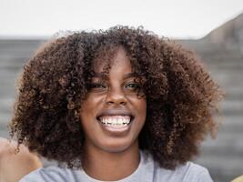 ritratto di contento afro americano alunno sorridente in il telecamera mentre seduta su di Università foto