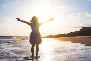 contento bambino diffusione sua mani su su il spiaggia su un' magnifico tramonto - bambino ragazza avendo divertimento nel vacanza vacanze - infanzia, figli, felicità concetto foto