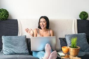 giovane donna fabbricazione video chiamata seduta su divano - contento ragazza avendo divertimento fare video conferenza con famiglia e amici - gioventù del Millennio persone stile di vita e tecnologia concetto foto