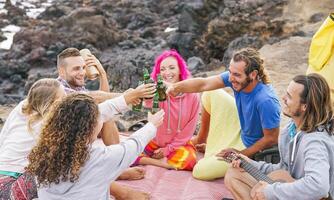 gruppo di amici applauso con birre su il spiaggia - contento persone godendo tempo insieme potabile, giocando chitarra e ascoltando musica con suono scatola - amicizia, vacanza, gioventù stile di vita concetto foto