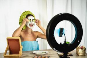 giovane femmina vlogger l'applicazione cura della pelle facciale maschera mentre streaming vivere per ragnatela canale a casa - contento ragazza avendo divertimento le riprese lezione con mobile smartphone - sociale influencer stile di vita concetto foto