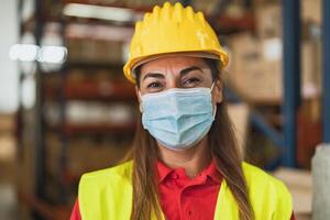 contento latino donna Lavorando nel magazzino mentre indossare viso maschera durante corona virus pandemia - logistica e industria concetto foto