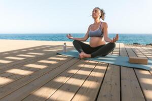 giovane incinta donna fare yoga sessione Il prossimo il mare - meditazione e maternità concetto foto