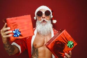 in forma anziano uomo avendo divertimento indossare Santa Claus Abiti e Tenere Natale regali durante vacanze foto