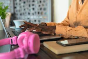 africano donna Lavorando su il computer portatile nel bar ristorante - lato Visualizza afro femmina mani digitando su computer - digitale nomade e libero professionista stile di vita concetto foto