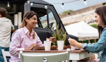 contento donne avendo un' pasto nel strada cibo camion mercato foto