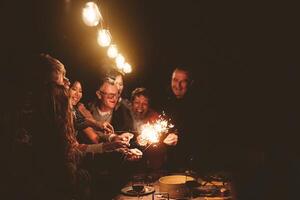 contento famiglia festeggiare vacanze con sparklers fuochi d'artificio a notte cena festa - gruppo di persone con diverso età e etnia avendo divertimento insieme foto