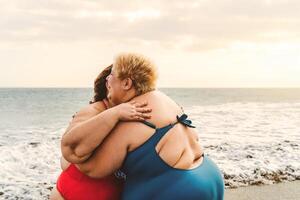 contento più dimensione donne abbracciare su il spiaggia - formosa sovrappeso ragazze avendo divertimento durante vacanza - al di sopra di dimensione fiducioso persone e amicizia concetto foto