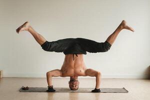 un' uomo con un' nudo torso fa yoga in piedi su il suo testa al chiuso. fitness allenatore foto