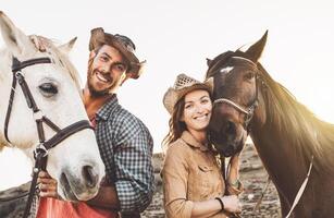 contento coppia avendo divertimento con cavalli dentro stabile - giovane agricoltori condivisione tempo con animali nel recinto per bestiame ranch - umano e animali relazione stile di vita concetto foto