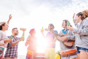 contento amici potabile birre e giocando chitarra a barbecue su il spiaggia - gruppo di giovane persone avendo divertimento e ridendo insieme a bbq festa - viaggiare, vacanza e gioventù vacanze stile di vita concetto foto