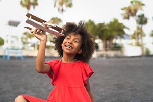afro bambino giocando con legna giocattolo aereo su il spiaggia - poco ragazzo avendo divertimento durante estate vacanze - infanzia e viaggio vacanza concetto foto