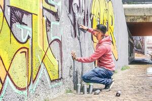 strada graffiti artista pittura con un' colore spray può un' buio mostro cranio graffiti su il parete nel il città all'aperto - urbano, stile di vita contemporaneo strada arte concetto - principale messa a fuoco su il suo mano foto