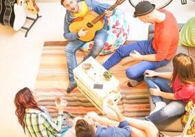 gruppo di amici giocando chitarra e potabile birra e whisky a casa - contento giovane persone incontro nel il vivente camera avendo un' divertente divertimento nel appartamento - gioventù, stile di vita, amicizia concetto foto