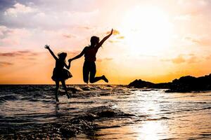 contento madre e figlia salto insieme lungo il mare acqua - silhouette di amorevole famiglia avendo divertimento su il spiaggia - le persone, vacanza e felicità concetto foto