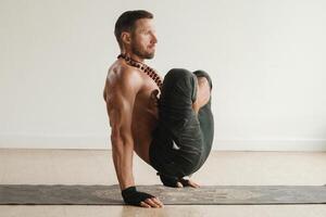 un' uomo con un' nudo torso fa yoga in piedi su il suo mani al chiuso. fitness allenatore foto