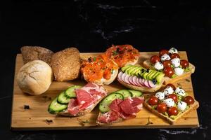 un assortimento di panini con pesce, formaggio, carne e verdure posare su il tavola e un' ciambella foto