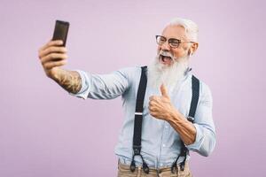 anziano uomo utilizzando mobile smartphone e ascoltando musica con airpods - contento maturo maschio avendo divertimento con nuovo tendenze tecnologia sociale media applicazioni - anziano stile di vita persone e Tech dipendenza concetto foto