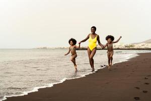 contento afro famiglia avendo divertimento in esecuzione su il spiaggia durante estate tempo - genitori amore e viaggio stile di vita concetto foto