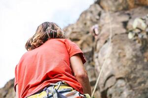 uomo e donna arrampicata su su montagna scogliera - scalatore nel azione su il roccia vicino il picco - concetto di estremo stile di vita, adrenalina e sport foto
