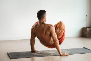 un' uomo con un' nudo torso fa yoga in piedi su il suo mani al chiuso. fitness allenatore foto