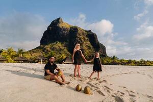 un' elegante famiglia nel nero Abiti con noci di cocco nel loro mani su il spiaggia di il isola di mauritius.bellissimo famiglia su il isola di mauritius nel il indiano oceano foto