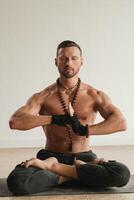 un' uomo con un' nudo torso è seduta nel il loto posizione prima fare yoga al chiuso. fitness allenatore foto