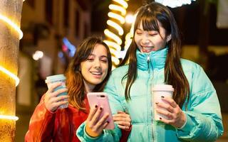 contento giovane donne utilizzando mobile smartphone mentre potabile prendere lontano caffè tazza all'aperto - amicizia e gioventù persone stile di vita concetto foto