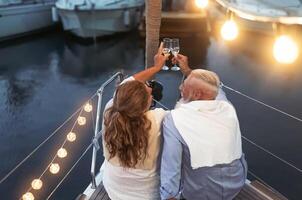 anziano coppia tostatura Champagne su barca a vela vacanza - contento maturo persone avendo divertimento festeggiare nozze anniversario su barca viaggio - amore relazione e viaggio stile di vita concetto foto