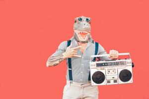 pazzo anziano uomo indossare t-rex maschera mentre ascoltando per musica Tenere Vintage ▾ Boombox stereo all'aperto - moda masquerade maschio avendo divertimento danza e festeggiare - assurdo e divertente persone concetto foto