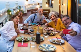 contento multirazziale anziano amici avendo divertimento cenare insieme mentre assunzione autoscatto con mobile smartphone su Casa terrazza - anziano stile di vita persone e cibo concetto foto