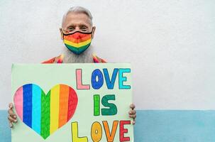 anziano gay uomo indossare viso protettivo maschera festeggiare gay orgoglio Festival durante corona virus scoppio - lgbt sociale movimento concetto foto