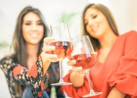 giovane donne tostatura bicchieri di rosa vino nel loro casa - contento ragazze godendo loro tempo insieme potabile cocktail e avendo divertimento ridendo - concetto di le persone, gioventù stile di vita - messa a fuoco su superiore bicchiere foto