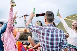 gruppo di amici applauso con birre a barbecue cena su il spiaggia - contento giovane persone campeggio con tenda e avendo divertimento a picnic cena - amicizia, festa e gioventù stile di vita vacanza concetto foto