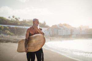 anziano maschio avendo divertimento fare surf durante tramonto tempo - in forma pensionato uomo formazione con tavola da surf su il spiaggia - anziano salutare persone stile di vita e estremo sport concetto foto