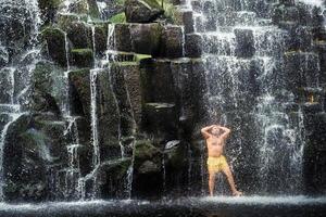 un' uomo sta sotto un' cascata nel il giungla. un' uomo a un' grotta cascata foto