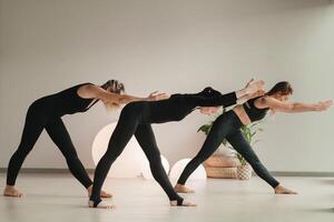 un' gruppo di ragazze nel nero fare yoga pose al chiuso. donne siamo impegnato nel fitness foto