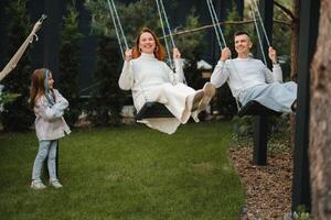 mamma e papà siamo equitazione su un' swing e Là è un' figlia in piedi Il prossimo per loro. il famiglia è riposo su un' swing foto