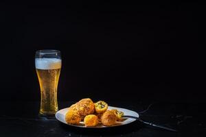 formaggio palle con aglio e aneto dentro per un' merenda con un' bicchiere di birra su un' nero sfondo foto
