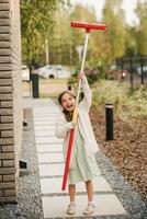 un' poco ragazza con un' spazzola pulisce un' sentiero su il strada nel il cortile foto