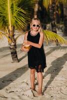 ritratto di un' allegro 9 anni ragazza con un' Noce di cocco cocktail su il sfondo di palma alberi su un esotico spiaggia.piccolo ragazza con un' Noce di cocco su il spiaggia di il isola di mauritius foto