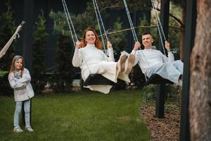 mamma e papà siamo equitazione su un' swing e Là è un' figlia in piedi Il prossimo per loro. il famiglia è riposo su un' swing foto